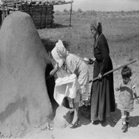 Dvije španjolske-američke žene postavljaju kruh u vanjskoj zemljanoj peći za istoriju pečenja